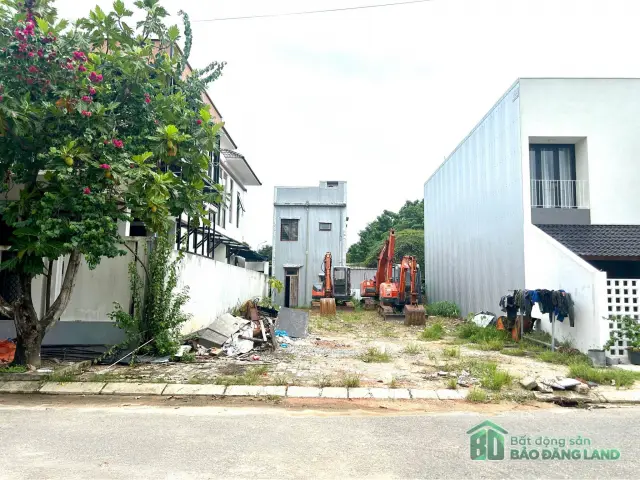 Lô đất trống đang san lấp với xe đào máy và đống vật liệu cũ phía trước