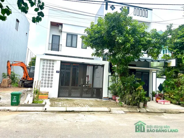 Căn nhà hai tầng sơn trắng có cổng sắt và cây xanh trước sân